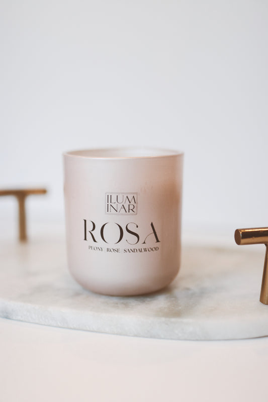 Iluminar Spring Limited Edition 'Rosa' Candle - 7.5 oz luxury coconut soy-based candle with crackling wooden wick in a pastel pink pearl-finished glass vessel. Features a woody floral scent profile with notes of rose, peony, and sandalwood. Hand poured, with a burn time of 60-70 hours